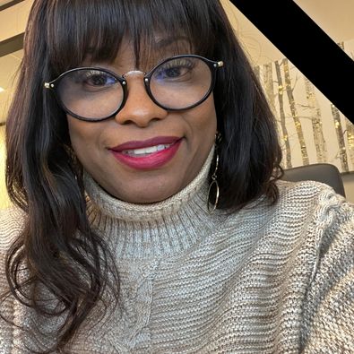 Felicia Barras A woman wearing glasses and a beige knit sweater smiles at the camera. A black diagonal ribbon appears in the top right corner of the image.